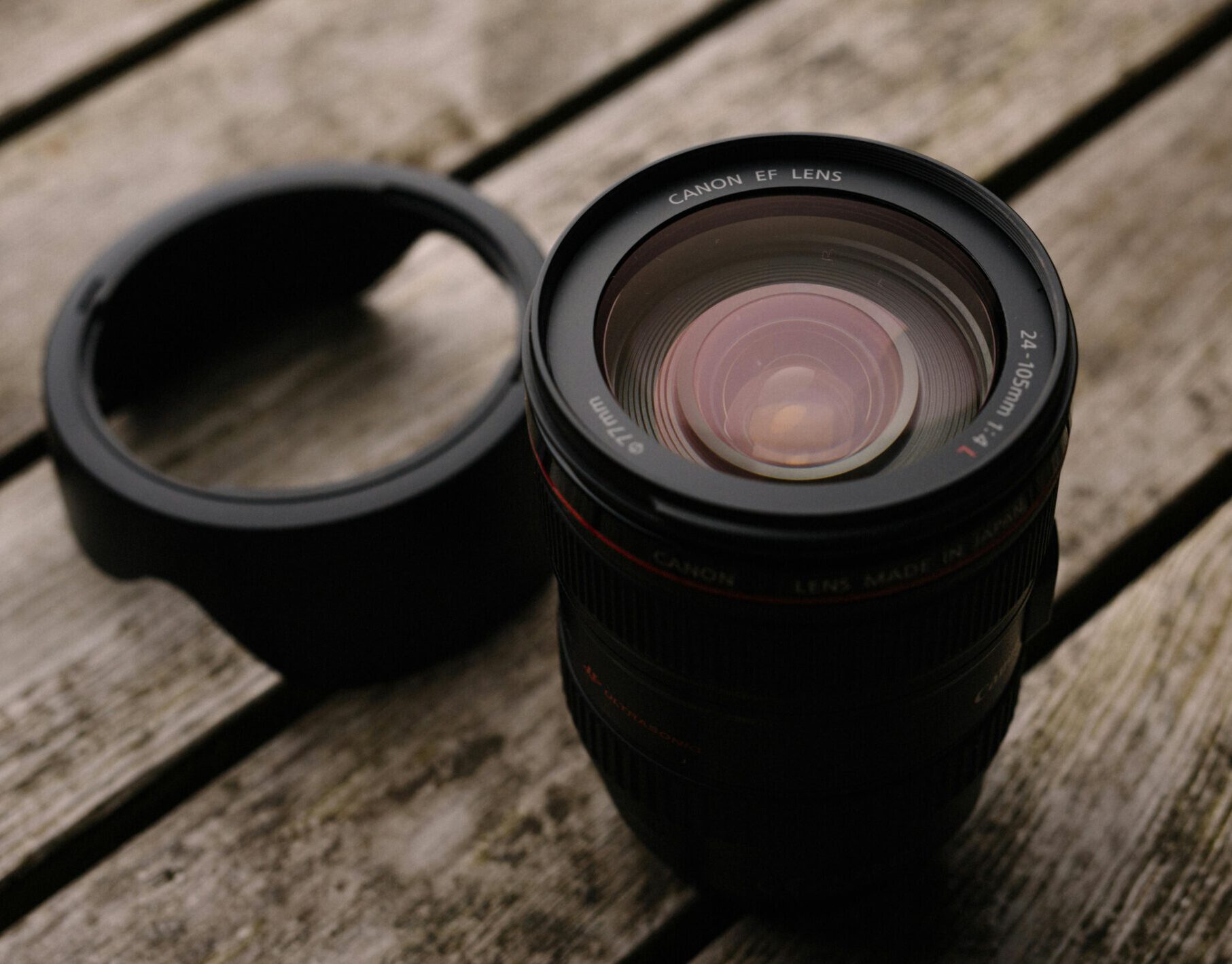 Close-up of a Canon EF lens with hood on a rustic wooden table, ideal for photography themes.