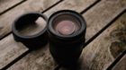 Close-up of a Canon EF lens with hood on a rustic wooden table, ideal for photography themes.